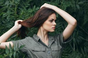 Frau berühren das Haar auf Ihre Kopf mit Ihre Hände im Wald Grün Blätter foto