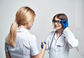 das Krankenschwester schüttelt Hände mit das geduldig auf ein Licht Hintergrund und Blau Handschuhe mit ein Stethoskop foto