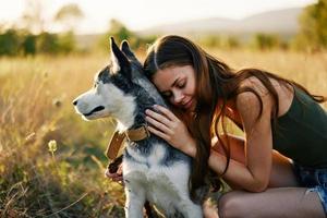 Frau lächelnd und umarmen ihr Hund Sitzung im ein Feld mit ein Dackel Hund lächelnd während Ausgaben Zeit draußen mit ein Freund Hund im Herbst beim Sonnenuntergang während Reisen foto