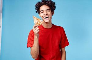 glücklich Kerl mit Scheibe von Pizza auf Blau Hintergrund lockig Haar Emotionen abgeschnitten Aussicht foto