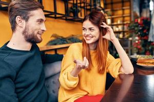 gut aussehend Mann und glücklich Frau im Sweatshirt sind Sitzung beim ein Tabelle im ein Cafe chatten Zimmer Innere foto