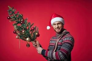 ein Mann im ein Santa Hut Weihnachten Baum Dekoration Spielzeuge rot Hintergrund foto