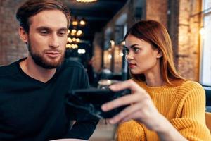 ein Frau im ein Sweatshirt mit ein Handy, Mobiltelefon Telefon und ein Kerl mit ein Bart sind Sitzung im ein Restaurant foto