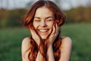 Porträt von ein jung rothaarig Frau suchen in das Kamera und lächelnd, Nahansicht Porträt von ein Lachen Frau im das Rahmen Sonnenlicht foto
