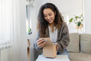 schön jung heiter asiatisch Frau Unboxing ein Paket im das Leben Zimmer von ein Neu Geschenk. foto