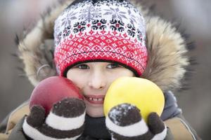 Kind im das Winter mit Frucht. das Junge im das Hut hält zwei groß Äpfel foto