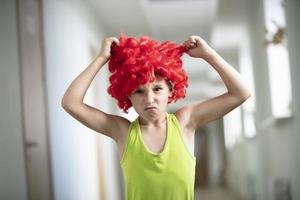 ein Kind im ein hell Perücke. komisch Junge mit rot künstlich Haar. tun nicht mögen das Frisur .. foto