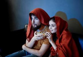 ein Mann und ein Frau mit ein rot Plaid auf ihr Köpfe sind Sitzung auf das Sofa im Vorderseite von das Fernseher drinnen foto