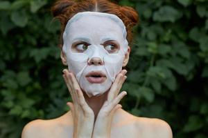 nett Mädchen kosmetisch Maske Verjüngung überrascht zu berühren Ihre Gesicht mit Ihre Hände Gebüsch im das Hintergrund foto
