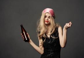 schön blond mit ein Flasche von Bier im ihr Hand und ein Rosa Maske auf ihr Kopf foto