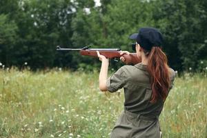 Frau Waffe Zielen Jagd zurück Aussicht auf draussen Grün Overall foto