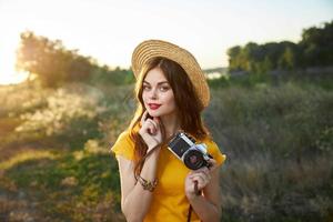 ziemlich Frau halten ein Kamera attraktiv aussehen rot Lippen Hut Natur foto