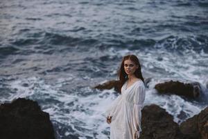 Frau im Weiß Kleid steht auf ein Cliff Lebensstil Stein Küste Landschaft foto