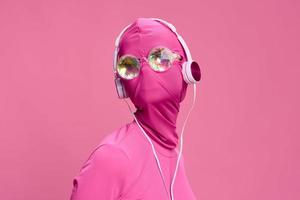 kreativ Ventilator Kunst Foto von ein jung weiblich Cyberpunk Blogger auf ein Rosa Hintergrund tragen ein Rosa Vollgesicht Maske mit glühend runden Brille und Kopfhörer