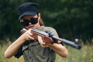 Militär- Frau Waffe im Hand Zielen Jagd Sonnenbrille Grün Blätter foto