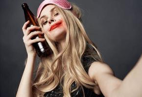 betrunken Frau mit ein Flasche von Bier auf ein grau Hintergrund Gesten mit ihr Hände und hell bilden foto