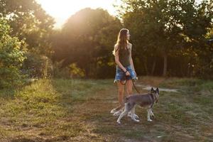 ein Frau läuft ihr zurück zu das Kamera mit ein Hund im das Wald während ein Abend gehen im das Wald beim Sonnenuntergang im Herbst. Lebensstil Sport Ausbildung mit Ihre Geliebte Hund foto