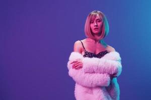 sexy blond Frau im flauschige Pelz Mantel prickelnd Kleid mit öffnen Schultern Kreuz Hände posieren isoliert im Blau violett Rosa Farbe Licht Studio Hintergrund. Neon- Party Mode Konzept. Kopieren Raum Banner foto