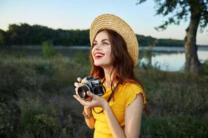 Frau im Natur Fotograf Kamera im Hände Lächeln aussehen oben Hut foto