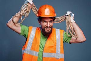 ein bärtig Mann Konstruktion Arbeiter im ein Orange schwer Hut Sicherheit Seil im seine Hände foto