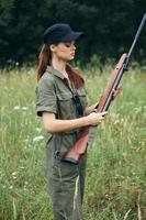 Frau sieht aus beim das Gewehr Jagd Lebensstil Grün Overall schwarz Deckel foto