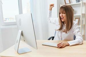 wütend böse blond Geschäftsfrau schreiend zu Desktop zittern Faust beim Bildschirm Sitzung beim Arbeitsplatz im modern Büro. gereizt Direktor Arbeit auf Computer online im finanziell Konzern. Kopieren Raum foto