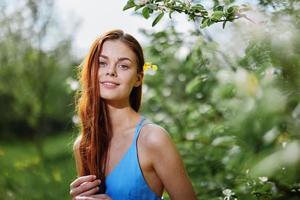 Porträt von ein Mädchen im Frühling und Sommer- in der Nähe von ein Grün Baum im das Park lächelnd im ein Blau Kleid Zärtlichkeit und Schönheit foto