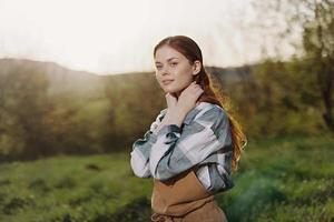 Porträt von ein jung lächelnd Frau im Arbeit Kleider kariert Hemd und Schürze im Natur im das Abend nach Arbeit foto