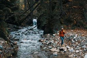 Frau Reisen durch das Fluss im das Berge und ein Rucksack auf ihr zurück transparent Wasser Wald foto