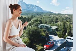 ziemlich Frau bewundert das Aussicht von das Berge auf das öffnen Balkon von das Hotel posieren foto