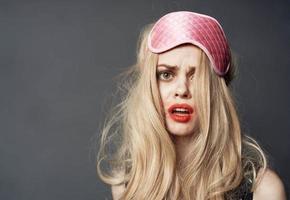 Porträt von ein blond im ein Schlaf Maske und hell bilden Lippenstift verschmiert auf ihr Gesicht foto