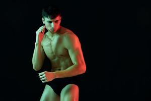 nackt Mann im kurze Hose posieren auf ein schwarz Hintergrund mit ein aufgepumpt Torso Bizeps Fitness Macho Muskeln foto