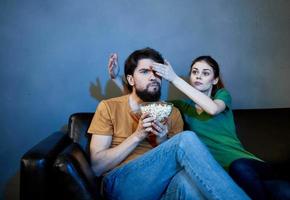 emotional Frau und Mann mit ein Teller von Popcorn Aufpassen Fernseher im das Abend drinnen foto