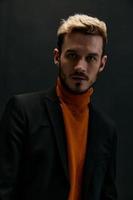Porträt von ein Mann im ein Mantel und ein Orange Sweatshirt blond dunkel Hintergrund Nahansicht foto