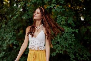 ein Frau im umweltfreundlich Kleidung im ein Hippie aussehen Tänze im Natur im das Park und lächelt beim das Welt. das Konzept von Harmonie mit das Körper und das Umgebung Natur foto