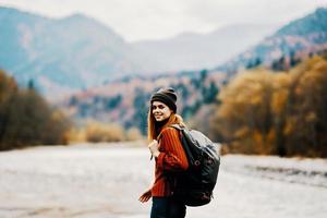 Frau Reisender mit ein Rucksack und im ein Hut in der Nähe von das Fluss im das Berge im Herbst foto