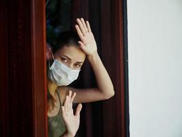 Frau halten Hände auf Fenster tragen Sperrung medizinisch Maske foto