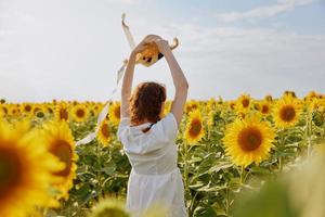 Frau mit angehoben oben Hände im ein Feld von Sonnenblumen Stroh Hut Landschaft Natur foto