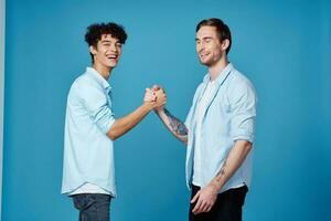 glücklich freunde im identisch Hemden Shake Hände auf ein Blau Hintergrund Kommunikation foto