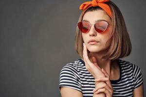 Frau im Sonnenbrille mit ein Orange Binde auf ihr Kopf im ein gestreift T-Shirt Mode foto