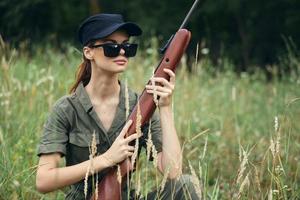 Frau Sonnenbrille mit Waffen im Hand Jagd Lebensstil schwarz Deckel Grün foto