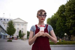 Frau mit kurz Haar auf das Straße tragen Brille Glas mit trinken gehen foto