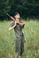 Frau auf draussen Frau mit ein Gewehr auf ihr Schulter Grün Overall frisch Luft Jagd Grün Blätter foto