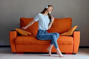 lächelnd Frau Sitzung auf das Couch beim Zuhause Hören zu Musik- auf Kopfhörer unverändert foto