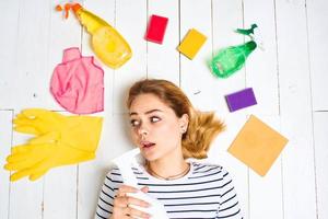 Frau im gestreift T-Shirt Lügen auf das Fußboden Reinigung liefert Waschmittel Hausarbeit foto