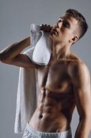 ein Kerl mit ein Handtuch im seine Hände Tücher aus das gepumpt oben Abs von ein Bodybuilder foto