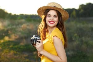 Frau Fotograf mit ein Kamera im ihr Hände Lächeln rot Lippen Gelb T-Shirt Hut gehen foto