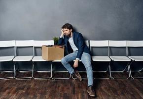 Mann sitzt auf ein Stuhl Box mit Dinge entlassen Unzufriedenheit Depression foto