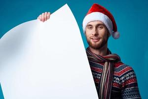 gut aussehend Mann im ein Santa Hut halten ein Banner Urlaub Blau Hintergrund foto