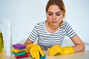 Reinigung Dame Sitzung beim das Tabelle mit Waschmittel Schwamm Gummi Handschuhe Hausarbeit Rendern Dienstleistungen foto